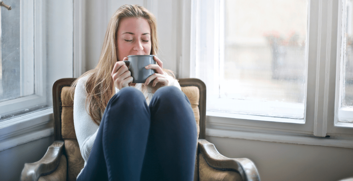 Person kneeling on chair drinking from mug