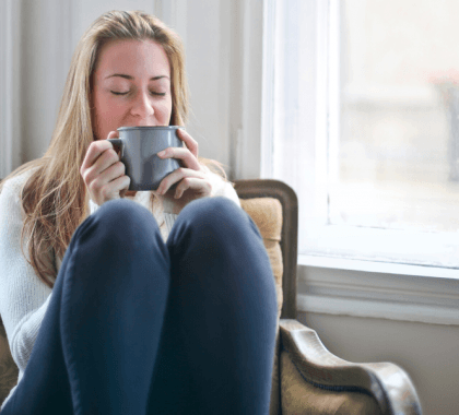 Person kneeling on chair drinking from mug
