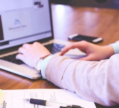 Person typing on laptop with mug and notes