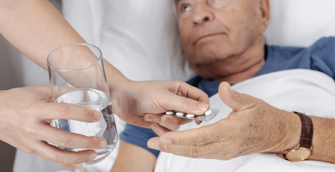 Carer handing medication to old man in bed