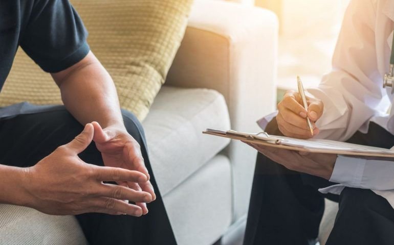 Man with hands pressed together consulting with clinician