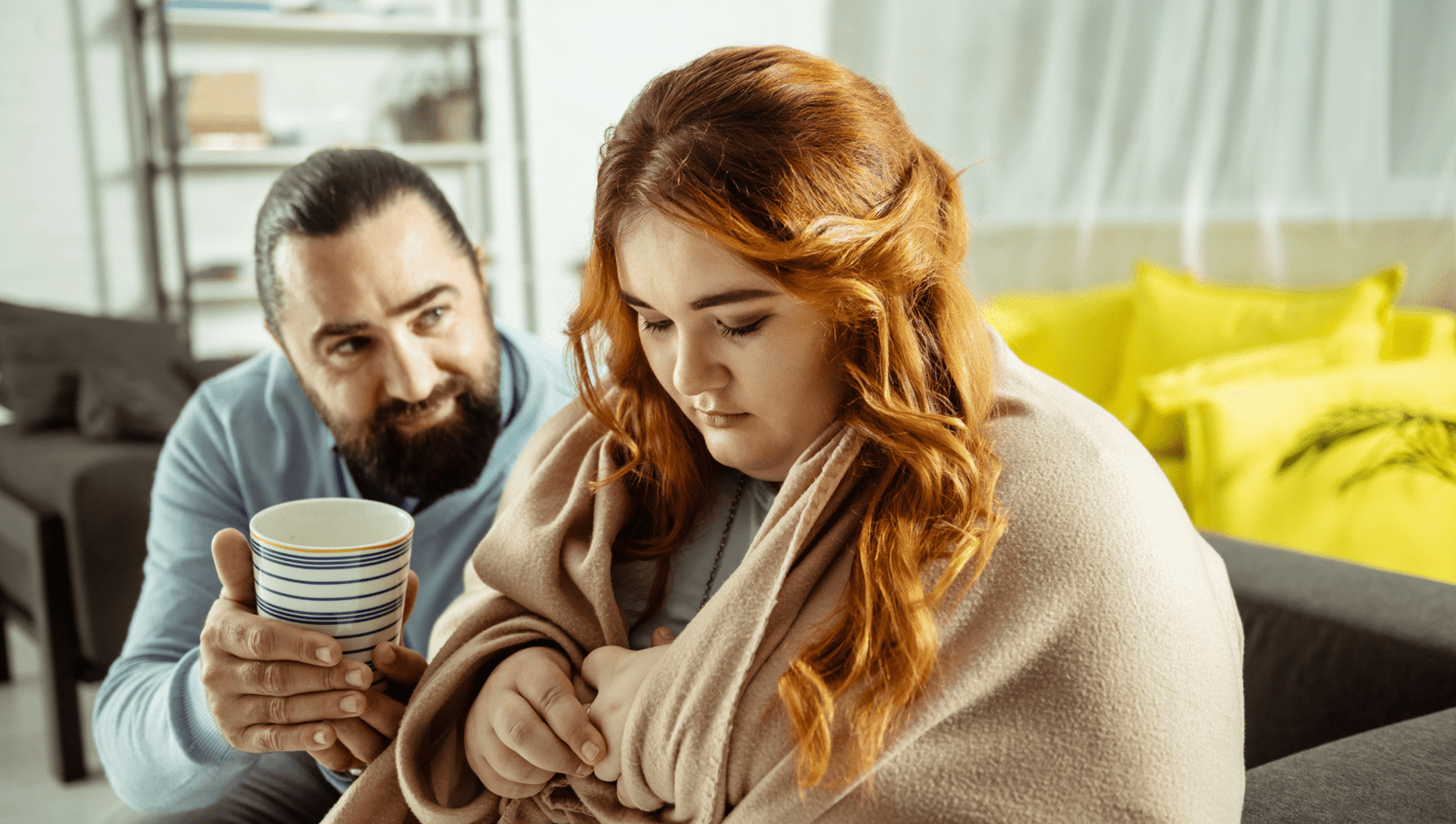 man comforting woman in blanket with mug