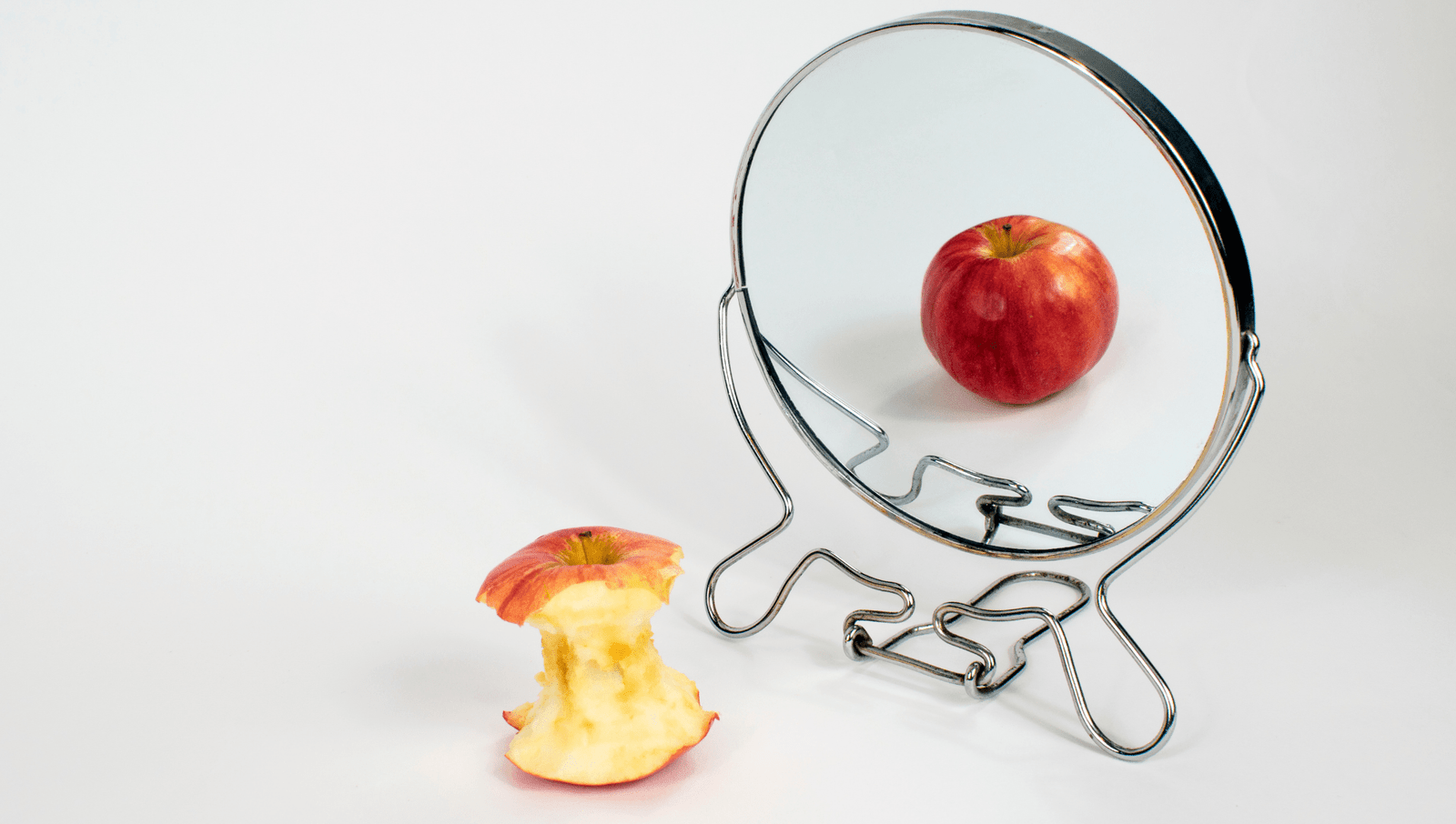 an eating apple next to a mirror where its reflection is a whole apple