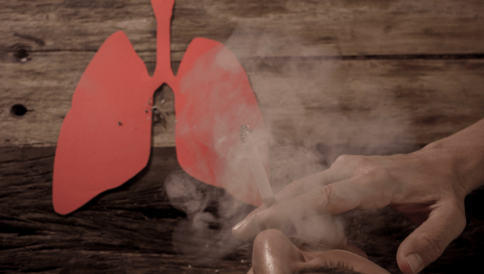 Person smoking onto red cardboard cutout of lungs